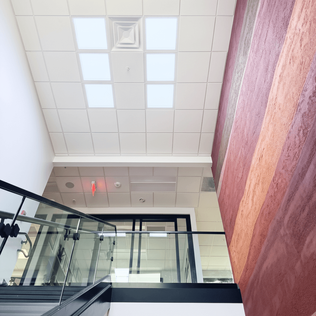 Circadian Sky panels installed in stairwell ceiling grid with glass railings and textured wall